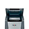 A grey paper shredder with the lid open, revealing a white sheet of paper. The Rexel logo is visible.