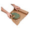 Des mains tiennent une assiette verte et du papier d'emballage. Une personne emballe l'assiette dans du papier brun.