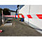 Ruban de signalisation rouge et blanc tendu devant un entrepôt sur un espace extérieur pavé.