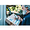 Ein Mann mit grauem Bart scannt einen Paketaufkleber mit einem Smartphone. Das Paket liegt im Laderaum eines Transporters.