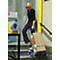 Woman pulls a cart loaded with packages up stairs. In the background an advertisement sign with a telecom logo.
