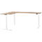 A corner desk with a light brown tabletop and white height-adjustable legs. The rectangular tabletop forms an L shape.