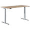 A height-adjustable desk with a light brown tabletop and silver legs. Controls for height adjustment.