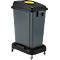 Grauer Abfallbehälter mit Deckel und Rollen. Oben ein gelbes Loch.