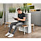 A man sits on a bench reading a magazine in a waiting area. Plants are behind him.