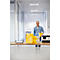 A man stands in the office. Stacks of paper and a printer are on a table.