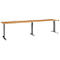 A long, light brown table with three black, height-adjustable legs, on a white background.
