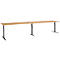 A long, rectangular desk with a light brown tabletop and gray, adjustable legs. Three pairs of legs support the tabletop.