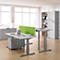 Bright office space with height-adjustable desks, laptop, file cabinet, green partition, and a view of a city.