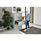 A woman in jeans and a denim jacket places a file in a gray filing cabinet. There is a houseplant next to the cabinet.