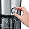 Close-up van een koffiezetapparaat. Een hand draait aan de zilveren draaiknop naast een glazen container met een waterniveau-indicator.