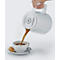 Eine weiße Kaffeekanne gießt Kaffee in eine Tasse. Auf dem Unterteller liegen Keks und Löffel.