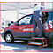 Mann auf roter Trittleiter, repariert rotes Auto. Auf dem Auto steht: "Diez Autohaus Trans Sport".