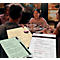Un groupe d'amis est assis à une table dans un restaurant. Il y a des menus sur la table. Une femme sourit gentiment à la caméra.