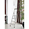 Aluminum step ladder against a white wall. A shelf on the left, a plant on the right. A decorative object hangs on the wall.