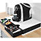 Coffee machine in action, black design, cup filling. Drawers with capsules and snacks. White shelf, wooden table.