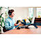Un homme avec un casque parle sur un ordinateur portable. Il est assis à une table en bois avec une souris et un clavier. Canapé et fenêtre en arrière-plan.