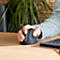 Gros plan sur une main utilisant une souris ergonomique. Le bras de l'utilisateur repose sur la table. Une plante est visible en arrière-plan.