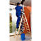 Ein Arbeiter in blauer Arbeitskleidung steht auf einer Holzleiter und arbeitet an einer Wand.