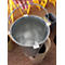 A person holds an empty metal bucket with a handle over a waste bin. In the background, yellow signs warning of slippery surfaces.