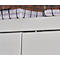 Close-up of white cabinet doors, a narrow silver metal trim and a wire basket with papers in the background.
