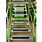 Metal staircase in a warehouse, with green railings and black anti-slip strips on the steps. Shelves in the background.