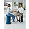 Two people sit on ergonomic stools in an office. They are talking, a woman is smiling.
