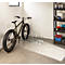 Un vélo est garé dans un garage devant un porte-vélos. Rangement d'accessoires sur une étagère.