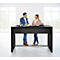 Un homme et une femme se tiennent à un comptoir de table haute noire, se parlent, bureau lumineux en arrière-plan.