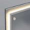 Détail d'angle d'un miroir éclairé. Un cadre blanc et rectangulaire entoure un éclairage LED lumineux et allongé. Au milieu, il y a un point lumineux rond.