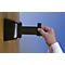 A hand holds a black belt lock. It is attached to a wooden wall with a black housing.