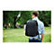 Ein Mann, der einen schwarzen Rucksack auf dem Rücken trägt, geht durch einen Park. Der Rucksack hat das Logo 'Targus'.