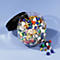 An open jar of colorful thumbtacks. Some lie beside.