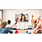 Children in classroom with raised hands. A girl is seen on the smartboard.