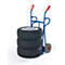 Three car tires rest on a blue hand truck with red handles. White background.