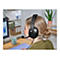 Eine Frau mit blondem Haar trägt ein schwarzes Headset. Im Hintergrund: Schreibtisch, Monitor mit Diagrammen und Büroregal.