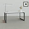 Bureau avec surface blanche, cadre noir, lampe et éléments décoratifs.