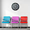 Three colorful chairs in front of a white wall, above a clock.
