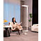 Femme lisant dans un fauteuil sous un lampadaire. Rideaux et canapé en arrière-plan. Ambiance chaleureuse.