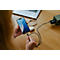 Person hält ein Smartphone, das an einem Kabel mit einem Ladestecker an einem Holztisch verbunden ist.