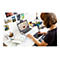 Junge Frau zeichnet am Schreibtisch auf einem Grafiktablett. Auf dem Laptop ist eine Comicfigur zu sehen.