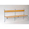Light wood bench on white wall. The bench has a backrest, a seat and metal supports.