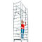 A woman in a red top stands on scaffolding, holding on. She's looking up.