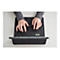 Nahaufnahme von Händen, die eine schwarze Tastatur bedienen. Die Person trägt einen grauen Pullover und Ringe an den Fingern. Die Tastatur ist mit einem Tablet verbunden und liegt auf einer weißen Oberfläche.