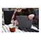 Une personne tenant un étui de tablette gris, à l'extérieur, à côté d'une tasse de thé.