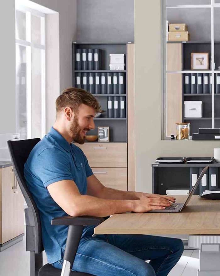 Un jeune homme est assis dans une posture saine et ergonomique sur une chaise de bureau.