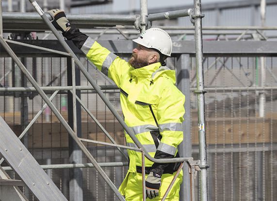Arbeiter auf einem Gerüst mit Schutzhelm, Warnkleidung und Schutzhandschuhen