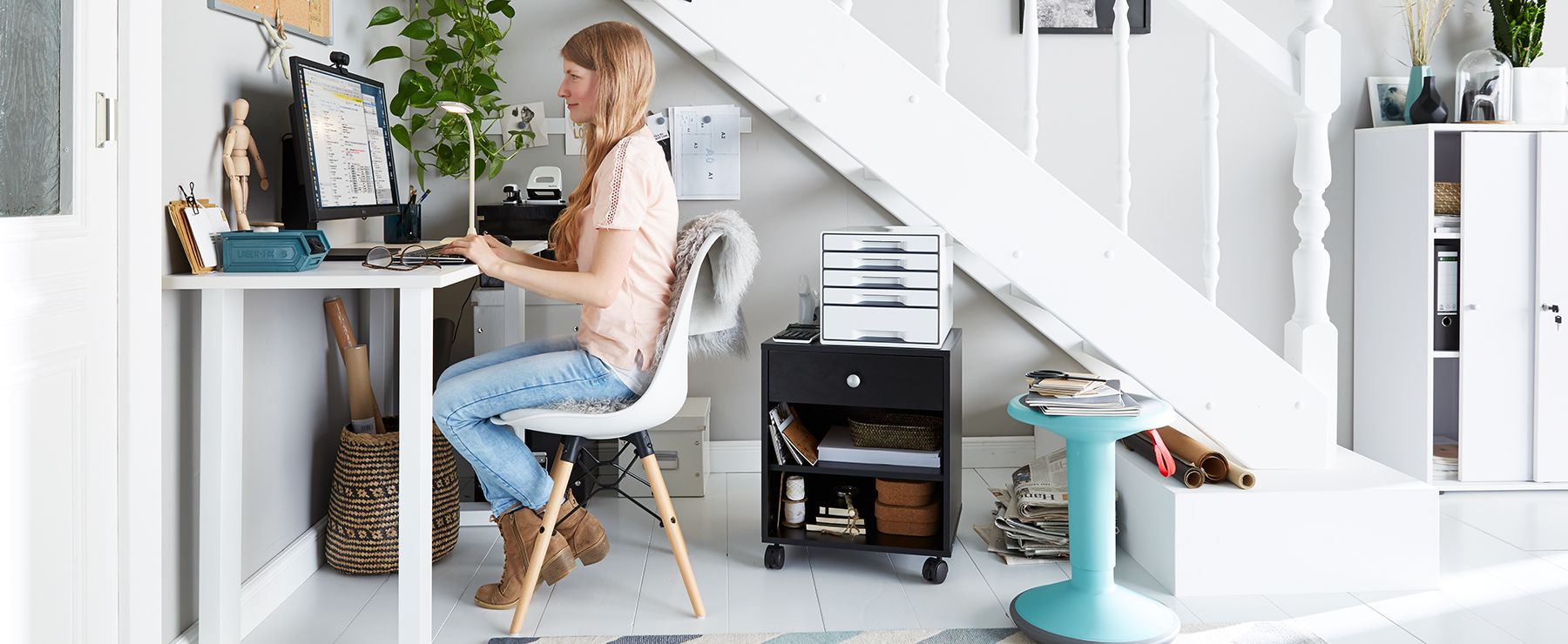 Vrouw werkt in een thuiskantoor in een kleine kamer met bureau, krukje en verrijdbaar ladeblok