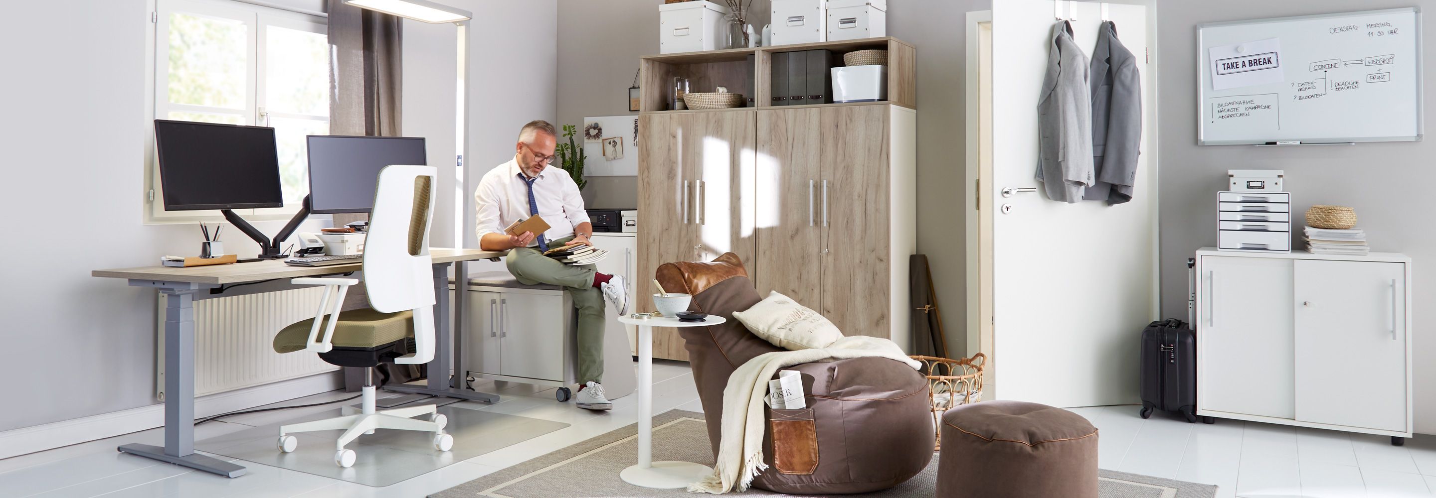 Ein Mann sitzt auf einerm kleinen Regal in seinem großen Büro und schaut sich Briefe an.