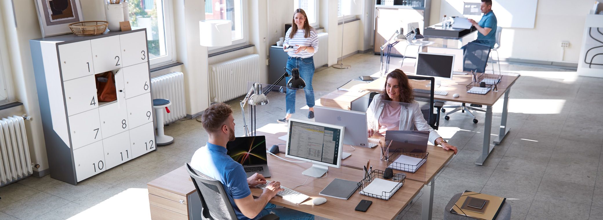 Büro mit flexiblen Desksharing-Arbeitsplätzen und vier Mitarbeitern.